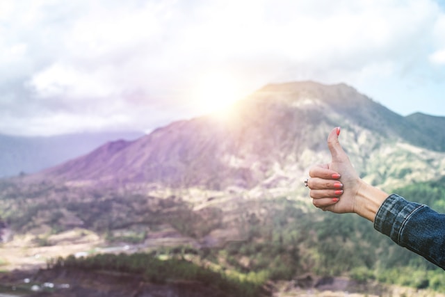 A woman thumbs up while in the background, a sunset in the mountains and valley bellow